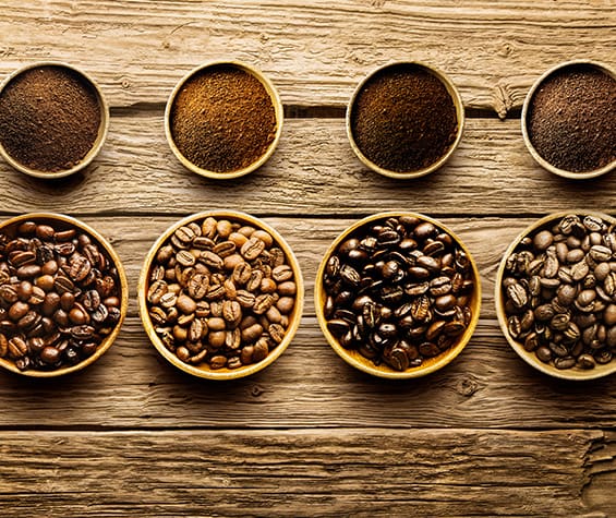 Leistungen Beispiel Kaffee Schritt 1 Wahl des Kaffees - mehrere Sorten Kaffee in Bohnenform als auch gemahlen in Schalen auf einem Holztisch