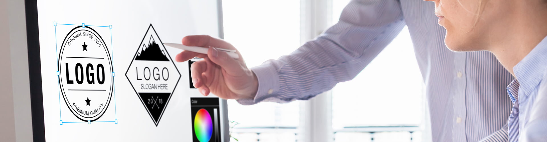 Mann mit Hemd zeigt mit einem Stift in der Hand einer Arbeitskollegin etwas an einem Logo auf einem Monitor